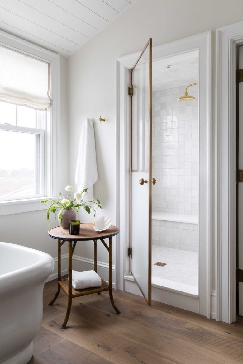 guest bathroom idea with a small round wooden table in a white bathroom with a pitched roof and large white-tiled walk-in shower