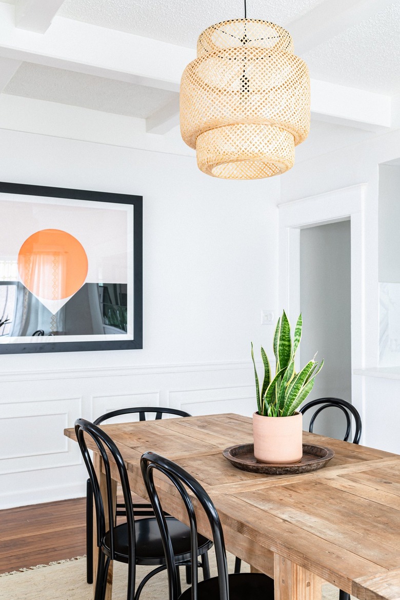 dining room wall decor idea with a wood dining table, snake plant, wicker pendant light and art