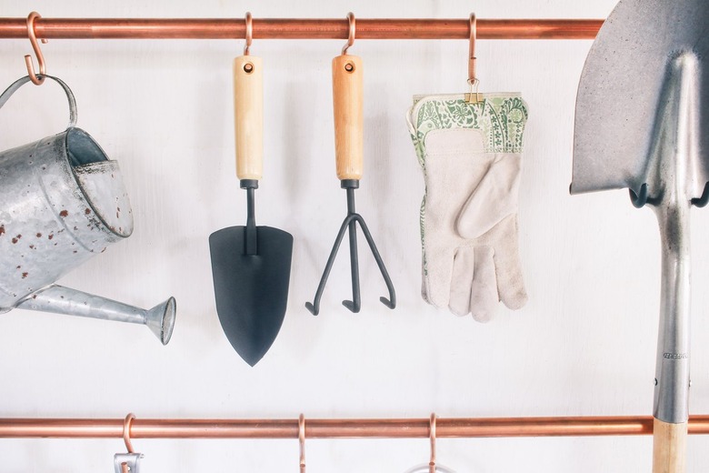 garage tools hanging on s-hooks that are suspended from copper pipes mounted on a wall