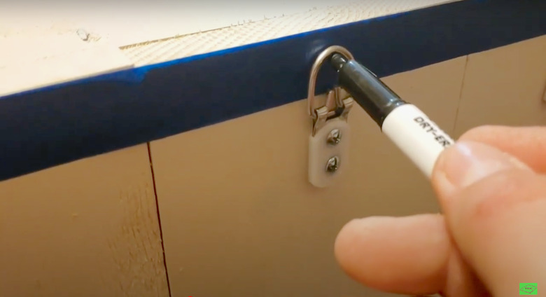 person marking hanging hardware on blue piece of masking tape