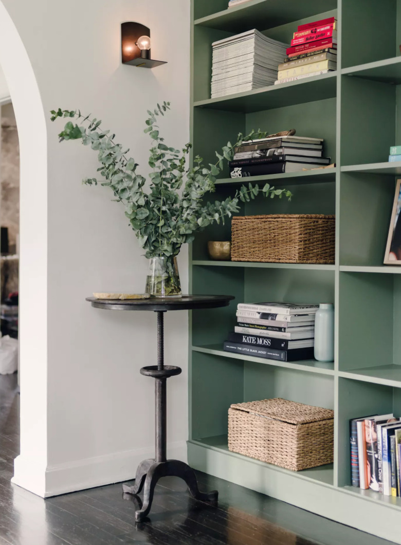 Hallway with round table, plant, bookshelves, sconce.