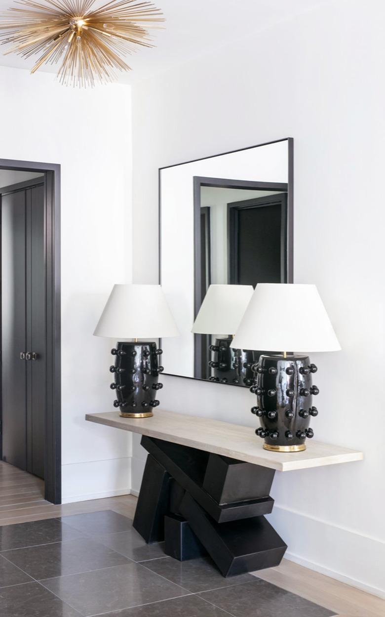 Entryway with pair of black and white table lamps, modern deco credenza, large mirror, gold pendant lamp.