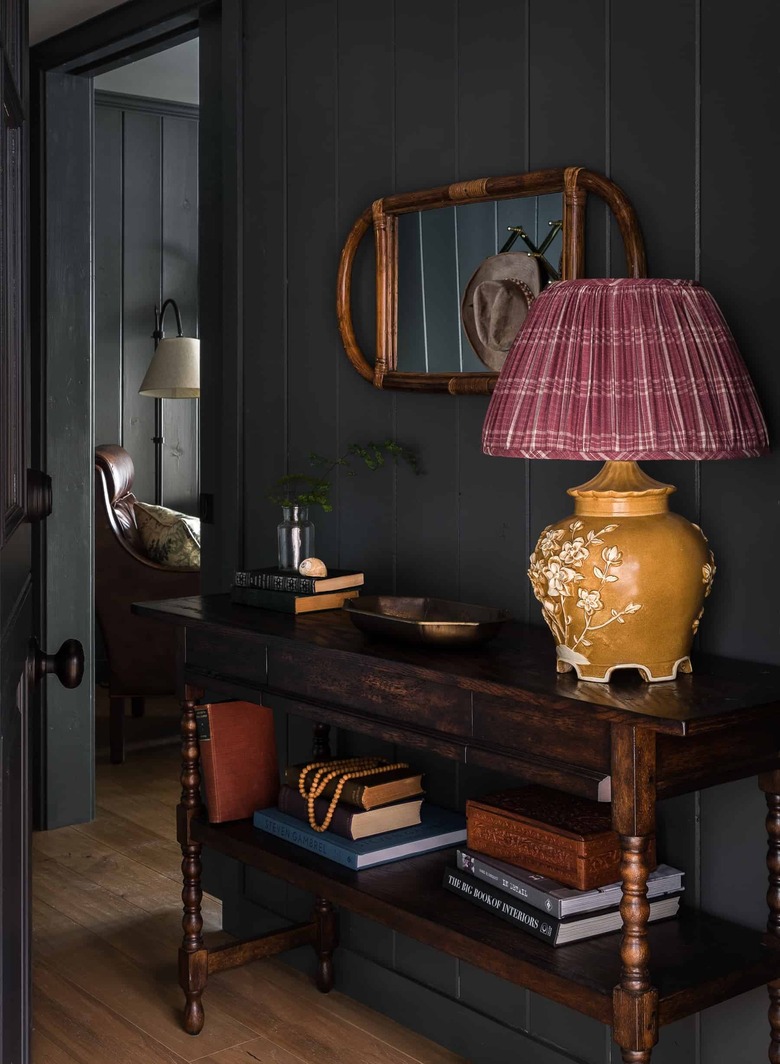 Entryway with shiplap, ceramic lamp with checked lampshade, credenza, books, cane mirror.