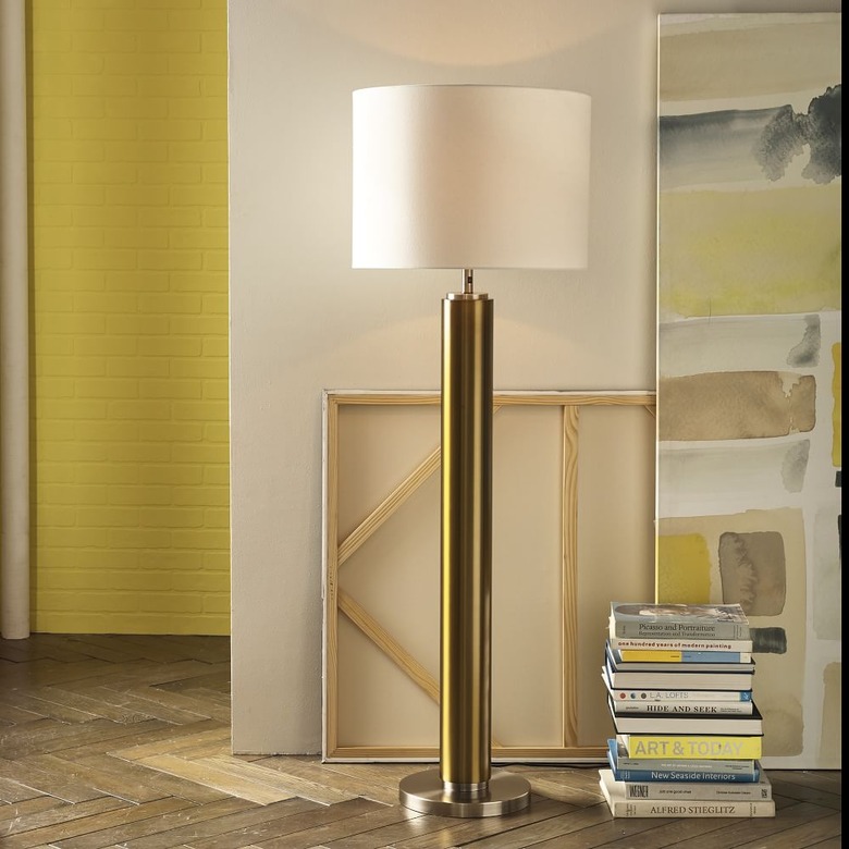 Floor lamp with brass base, white shade in hallway with books, art