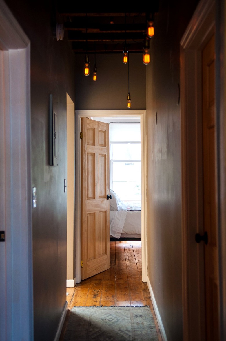 Hallway Lighting Ideas in a narrow hallway with dim pendant lights and a rustic pine floor opens into a bright bedroom