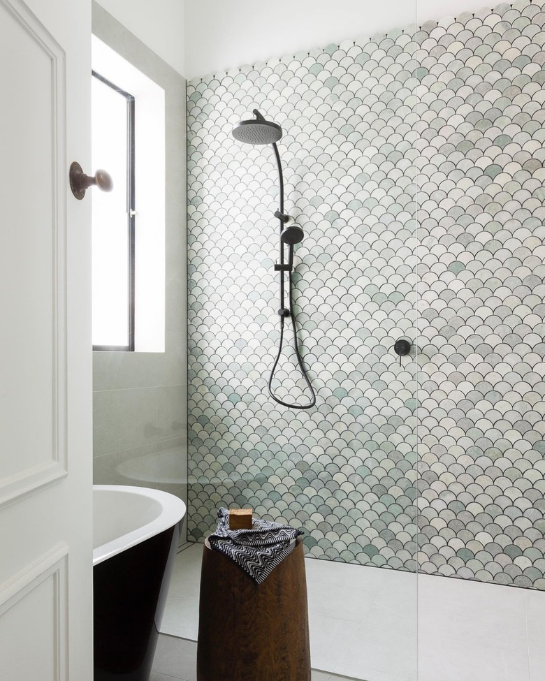 Handheld showerhead in walk-in shower with green mosaic wall tile and freestanding bathtub