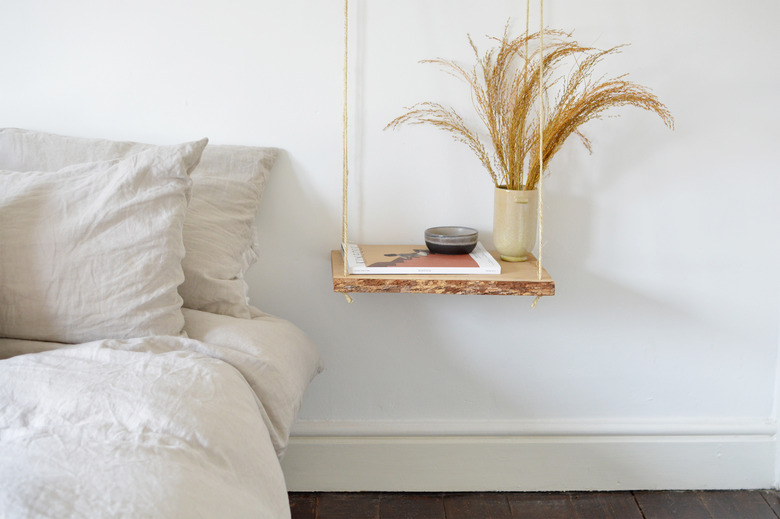 Floating wood nightand with dried grasses next to a neutral colured bed