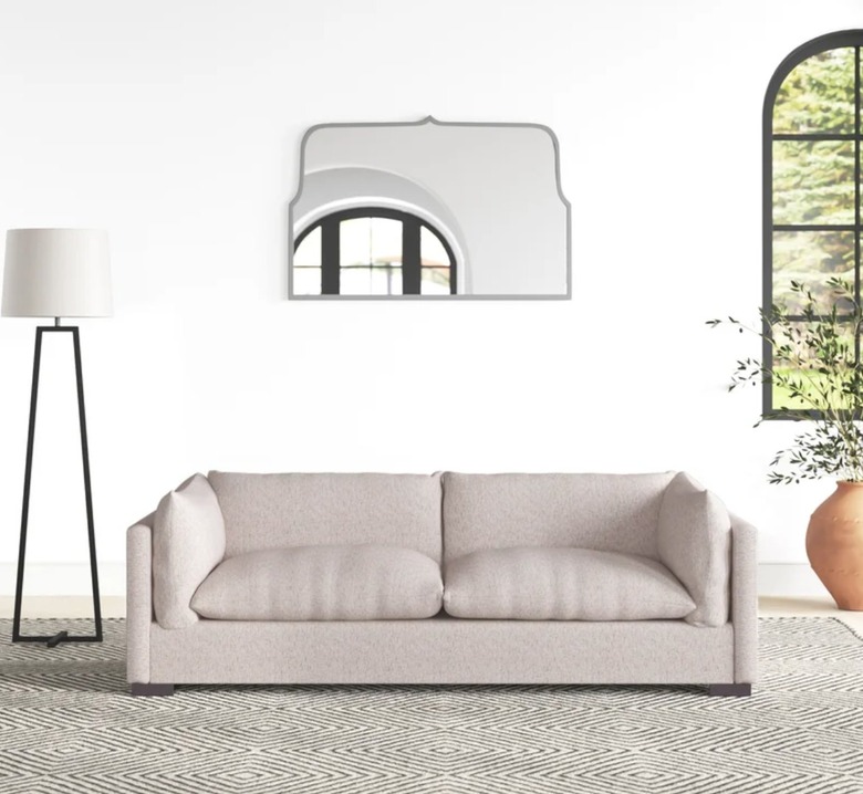 Living room with beige slipcovered sofa, floor lamp, mirror, rug.