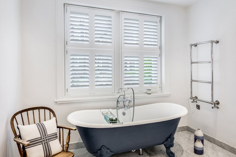 bathroom curtain idea with navy blue clawfoot tub in a white bathroom with white plantation shutters on the window