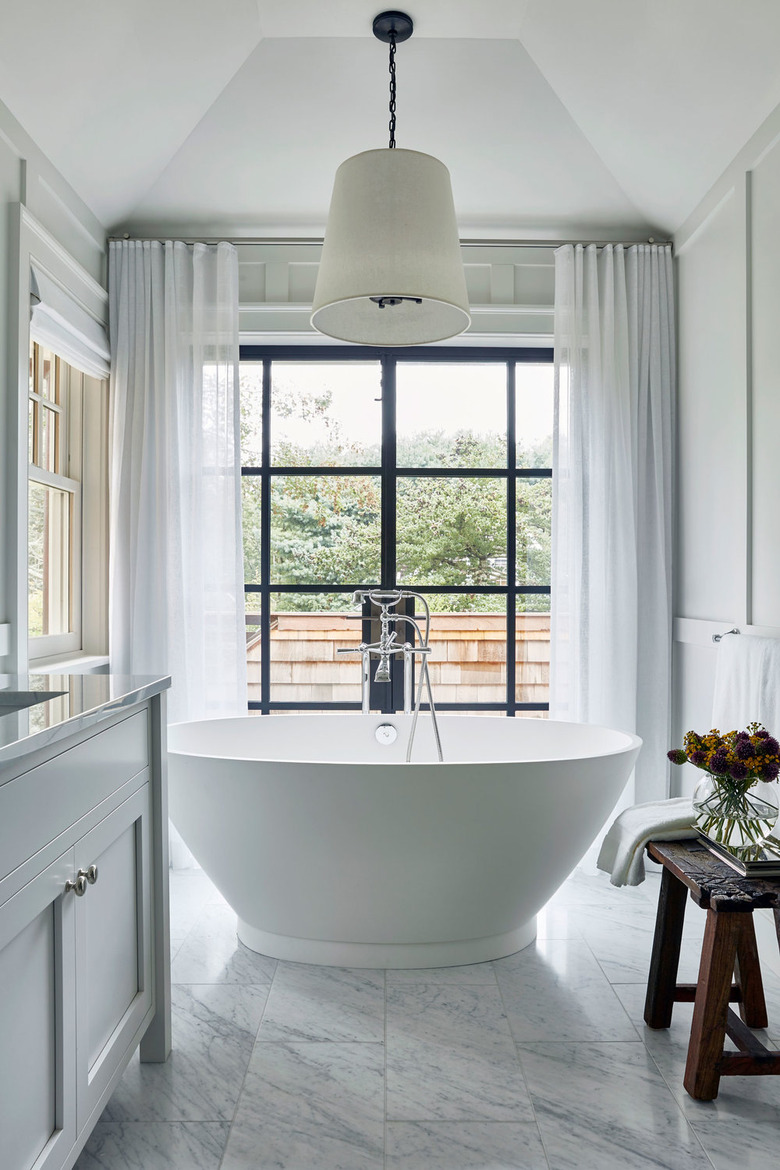 bathroom curtain idea with soaker tub in the middle of a large bathroom with marble tiles and a floor-to-ceiling window