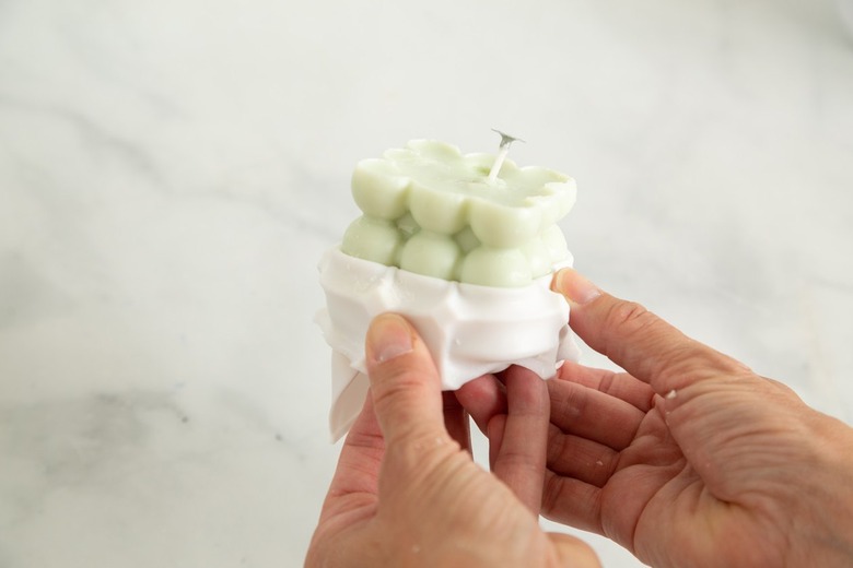 Person removing a pastel green, bubble cube candle from a plastic mold.