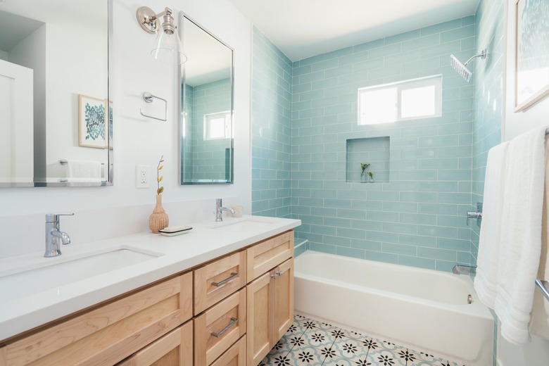 Bathroom with retro floral tile on floor, light blue subway wall tile in shower, light wood cabinet vanity with double sinks