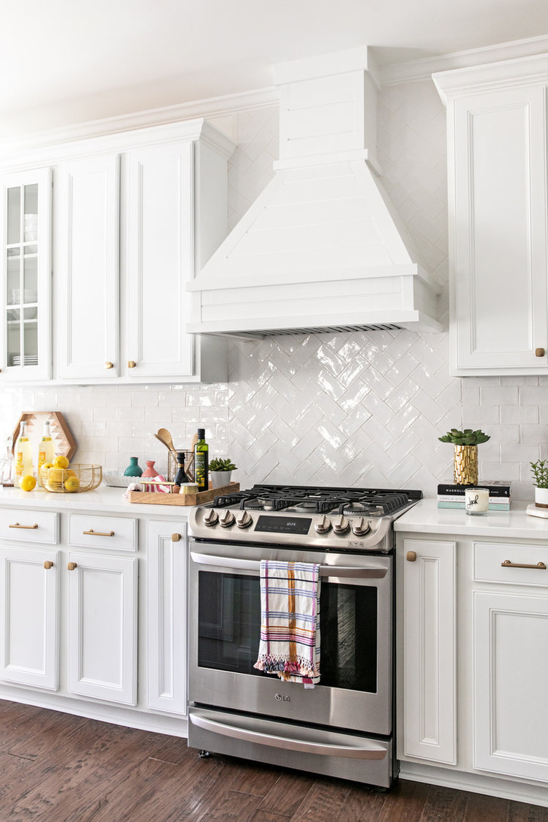 Shiny white herringbone backsplash with white cabinets and cooking tools