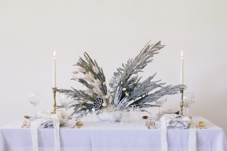 Glittery dried flowers and grass painted gray on table with dishware and candles