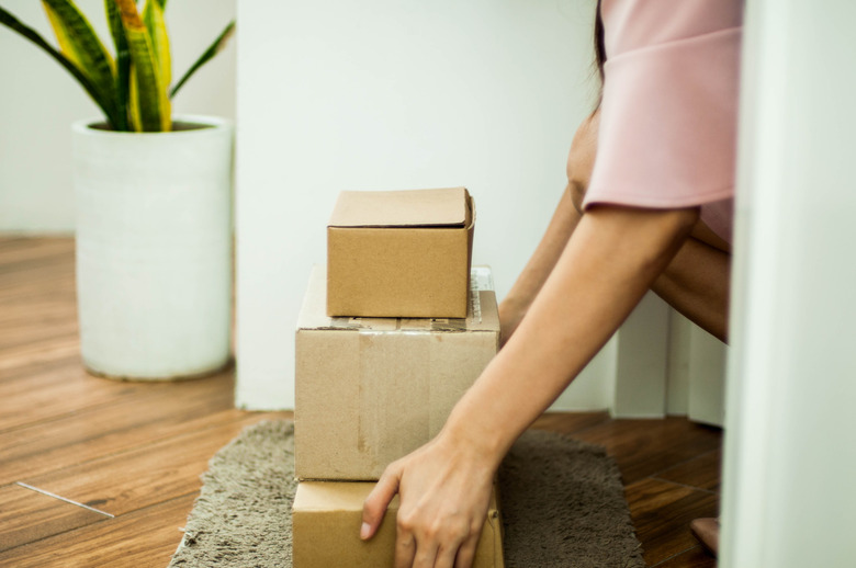 A young Southeast Asian woman is picking up carton packages on the front door