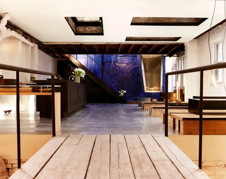 A bridge in a lofted apartment leading to a bed with a waterfall pouring out from under it.