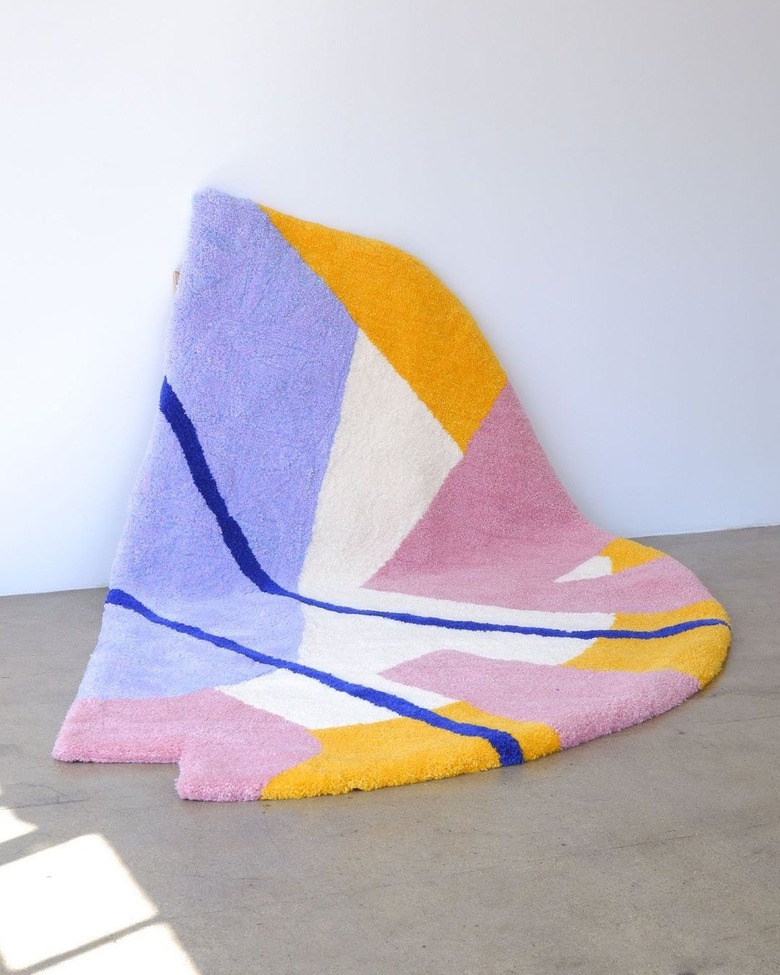 An irregularly shaped purple, cream, pink, yellow, and royal blue geometric rug.