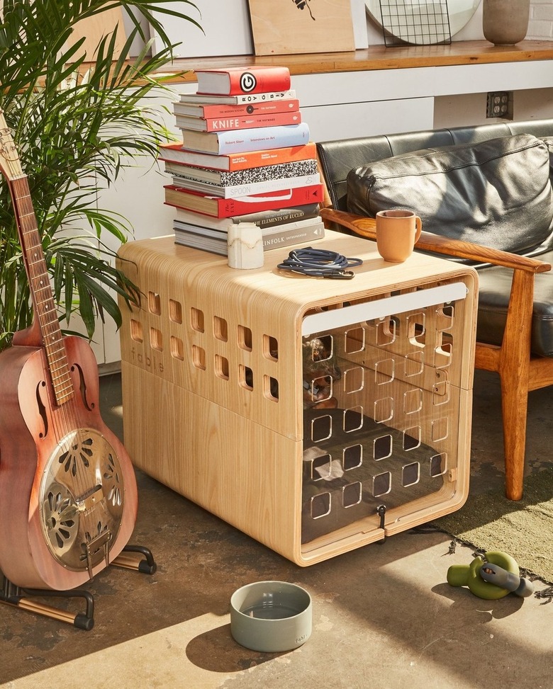 A light wood dog crate being used as a side table in a living room with a black leather sofa that has wood arms.