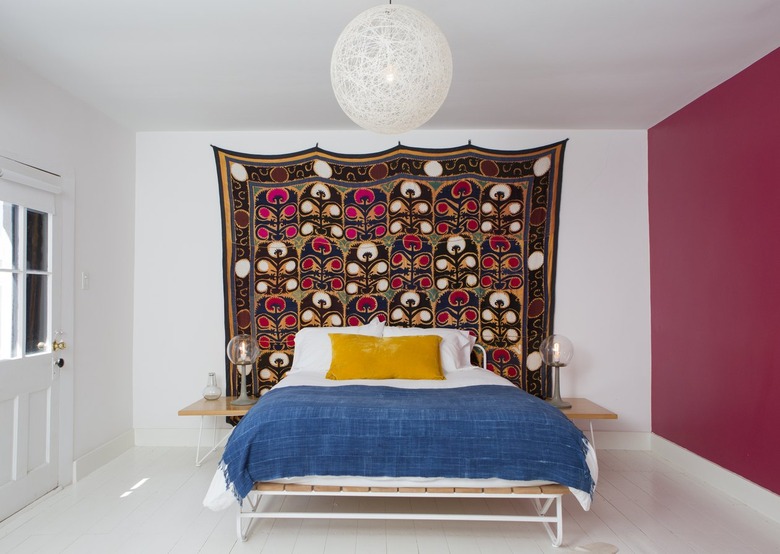 Colorful bedding, a wall tapestry and globe light in a bedroom with white-pink walls