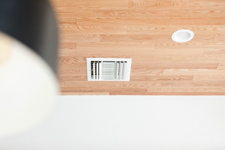 A blurred up close shot of a pendant light with a recessed light and ceiling fan on a wood ceiling in the background in focus.