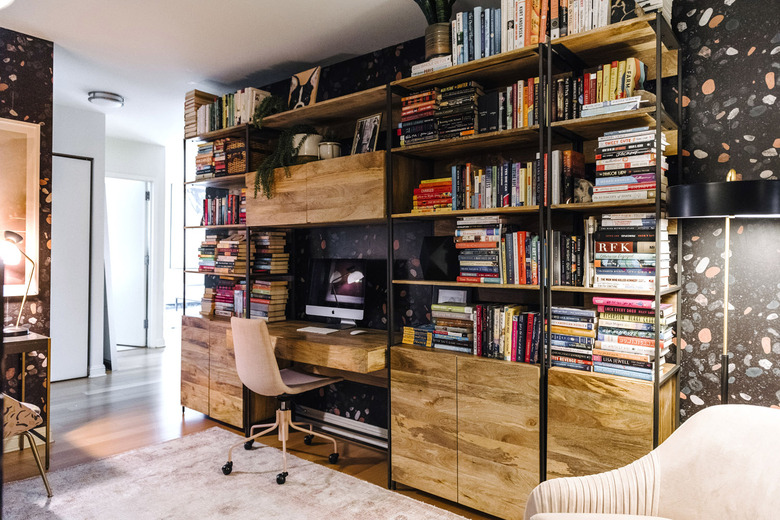 dark home office with a wall of industrial style bookshelves filled with books