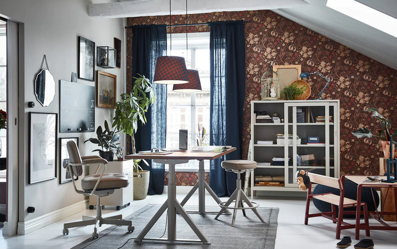 modern home office with wallpapered accent wall and desk in the center of the room with two pendants above it