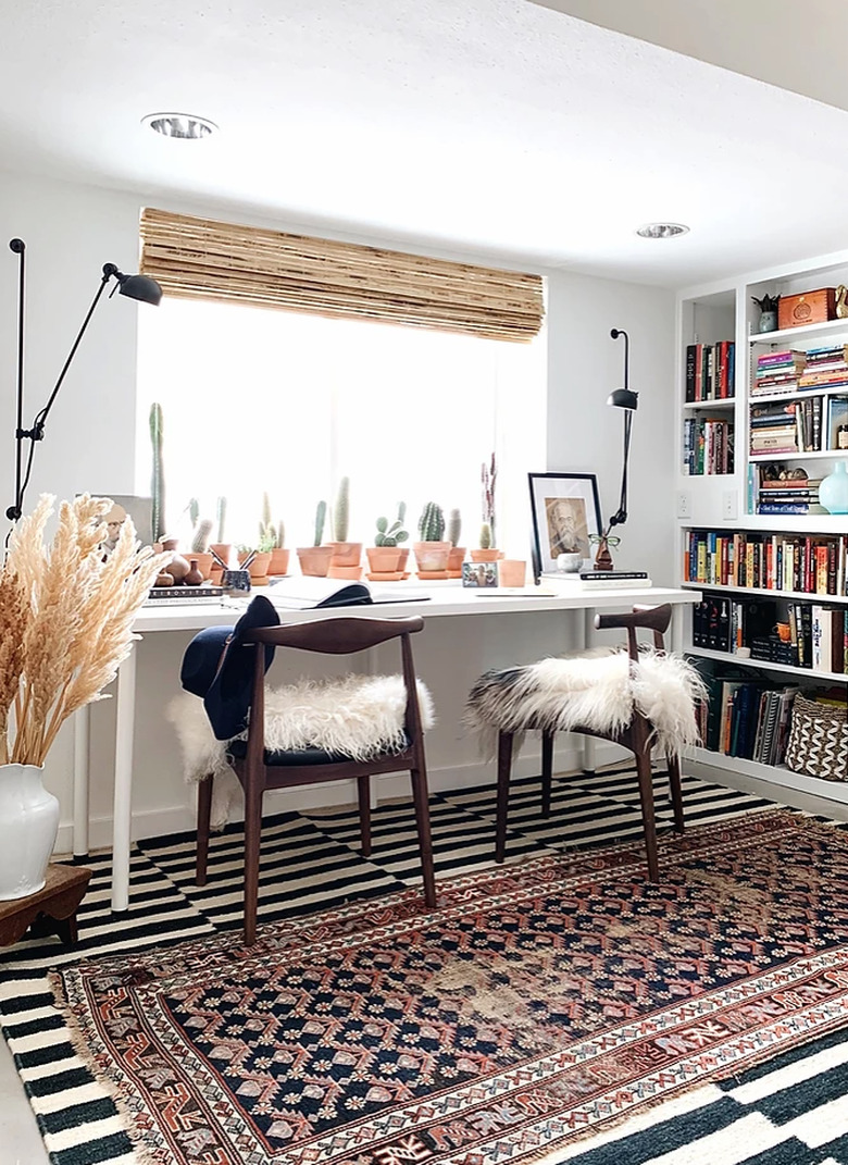 Home Office for Two Shared desk with layer area rugs, sheepskin on chairs, bamboo blind, cacti, bookshelves.