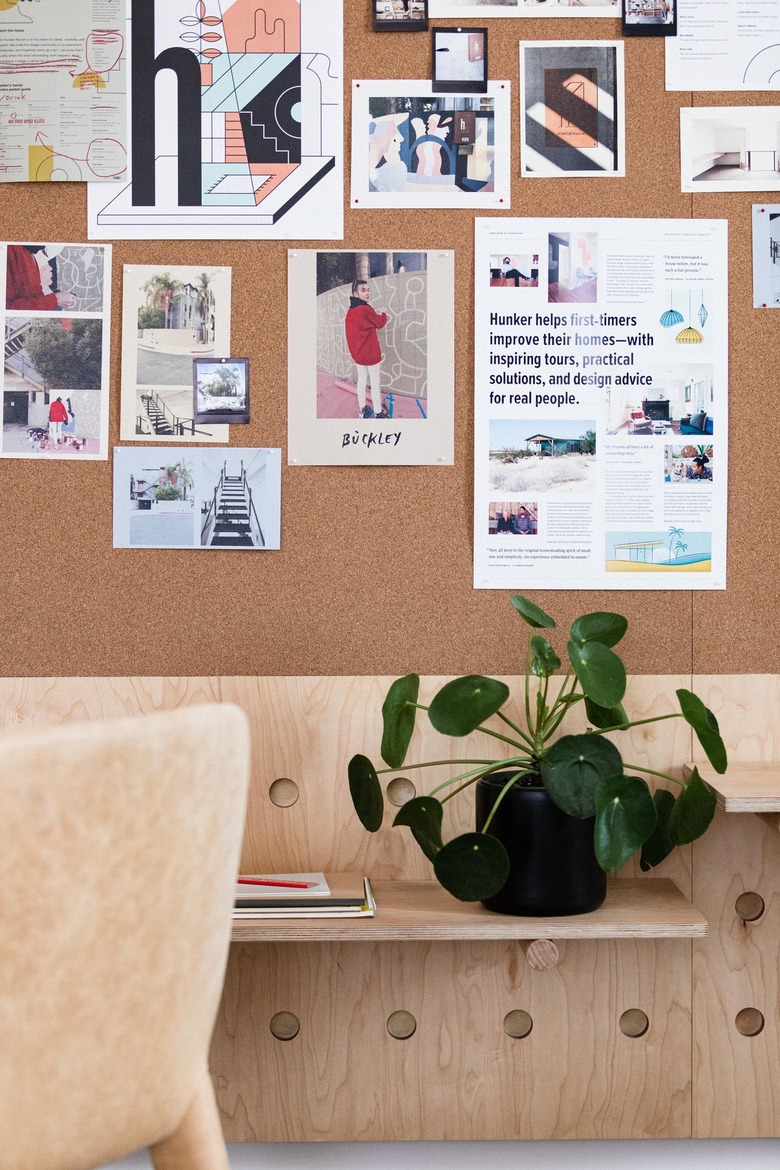 a corkboard above a plywood pegboard with shelves