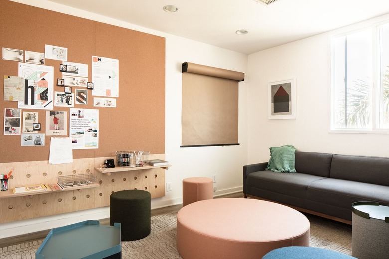 a sitting area with a gray couch, large round coffee tables, and a roll of butcher paper hanging on a wall