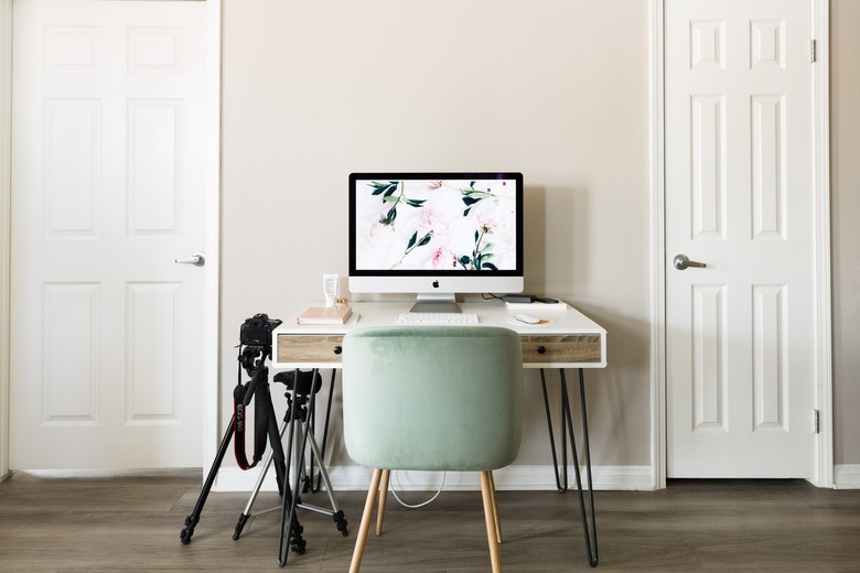 Green chair with wood legs at a wood hairpin leg desk with a desktop computer. Camera tripods are beside.