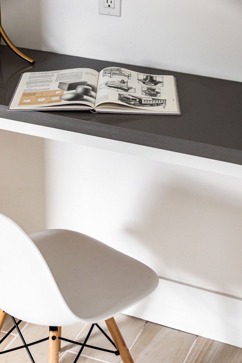 A white chair at a gray side table/desk and white walls