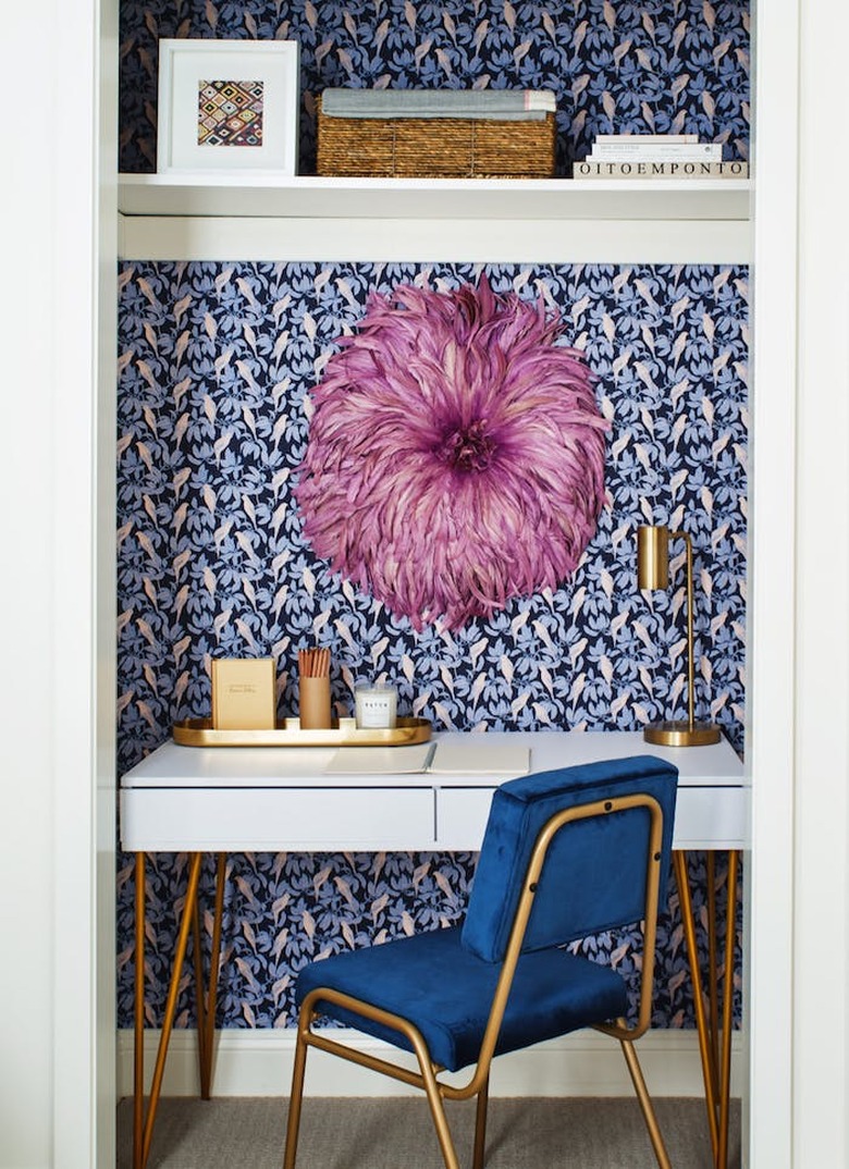 closet home office with blue parrot print wallpaper, blue velvet desk chair and large pink, feathered wall hanging