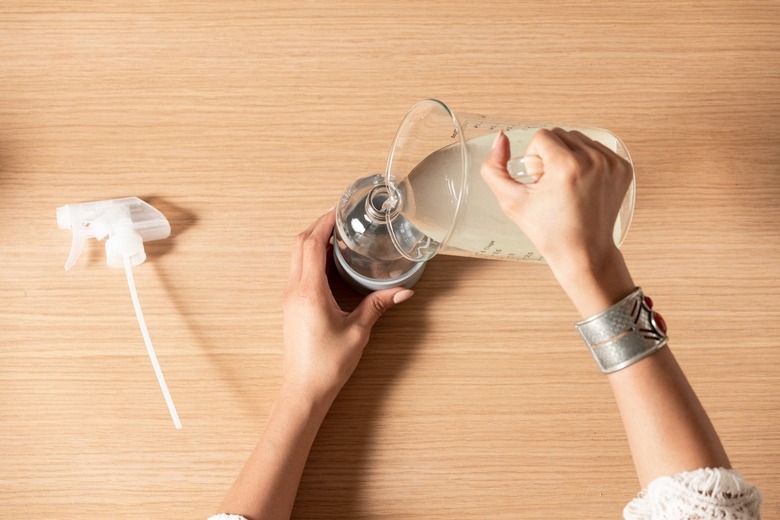 Hand pouring liquid from measuring cup into spray bottle on wooden countertop