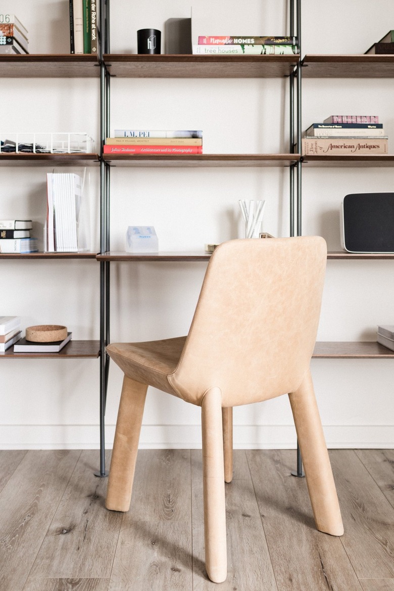 A peach-colored chair covered in soft material sits in front of a tall minimalist shelving unit