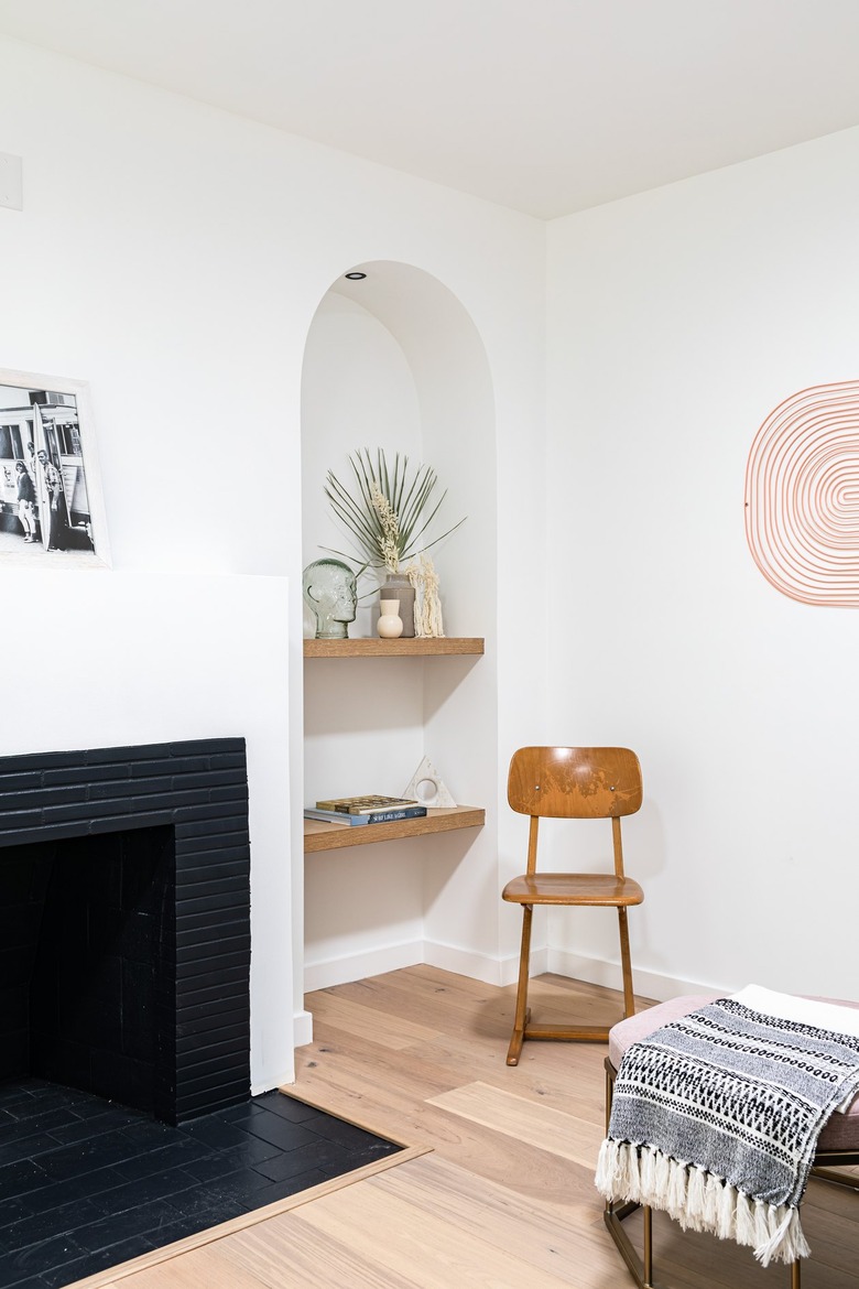 Corner of contemporary living room with black fireplace, alcove with wood shelves and plants, wood desk chair, and hung art