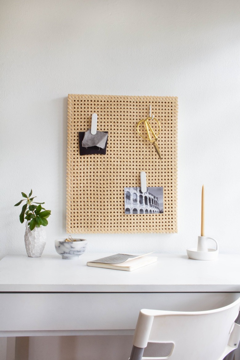 Cane memo board over white desk with plant and candle