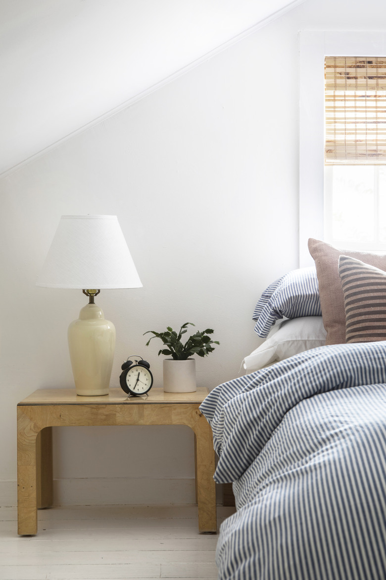 Blue and white striped bed cover; wood nightstand with yellow lamp