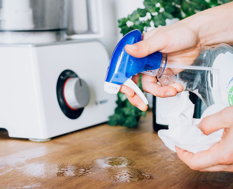 person spraying wood cutting board with cleaning product in spray bottle