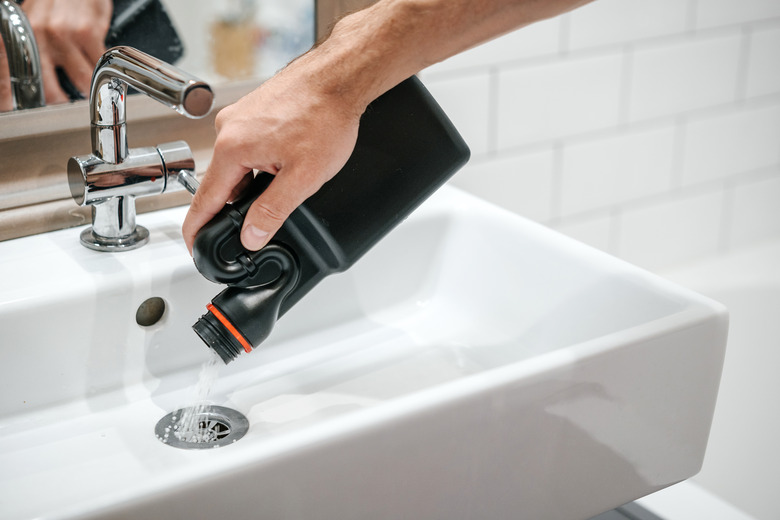 Removal of blockage in bathroom sink; the hand of a man pouring drain cleaner in a drain.