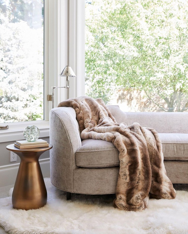 Curved taupe sofa with a brown faux fur throw on it