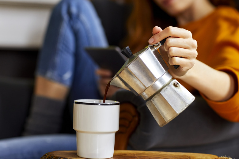 Young woman pouring coffee into cup at home