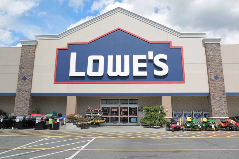 A Lowe's storefront with lawn mowers and flowers out front.