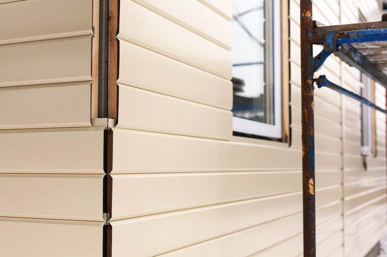 House corner with beige siding covering the walls and scaffolding. Focus on corner.