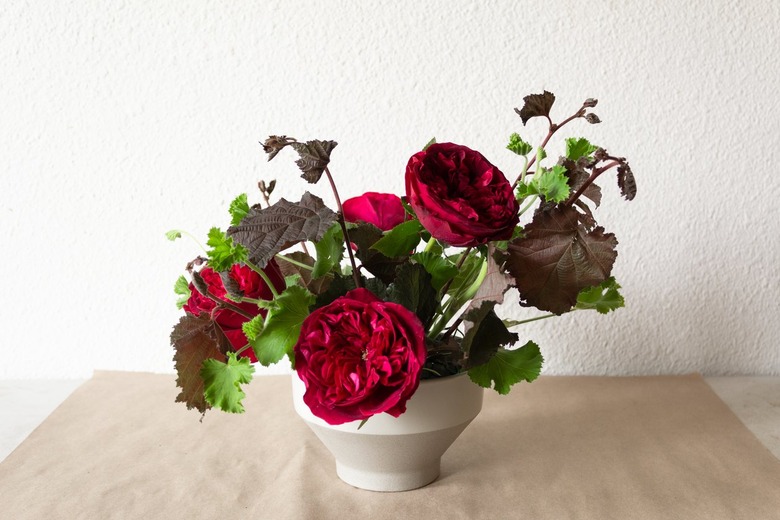 geranium, nine bark stems, and roses in a white vase