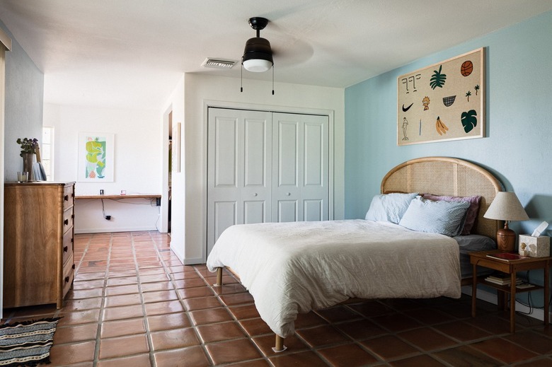 A black ceiling fan spinning above a rattan bed on a terra cotta floor