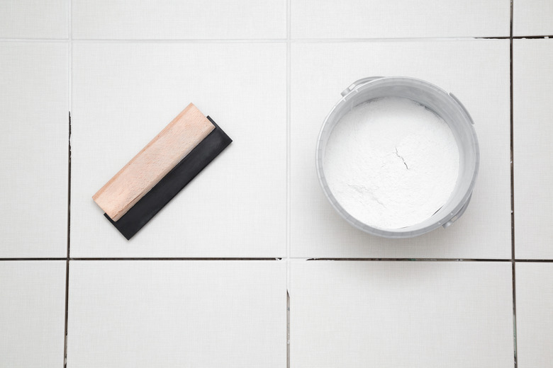 Rubber trowel and container with powder of grouting paste for ceramic tile seams on floor. Closeup. Top down view.