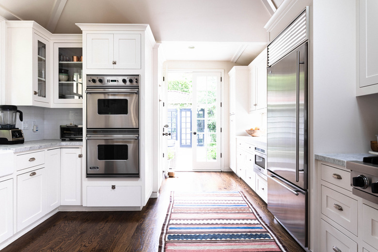 galley kitchen splitting a hallway leading outside, view of double ovens and striped rug