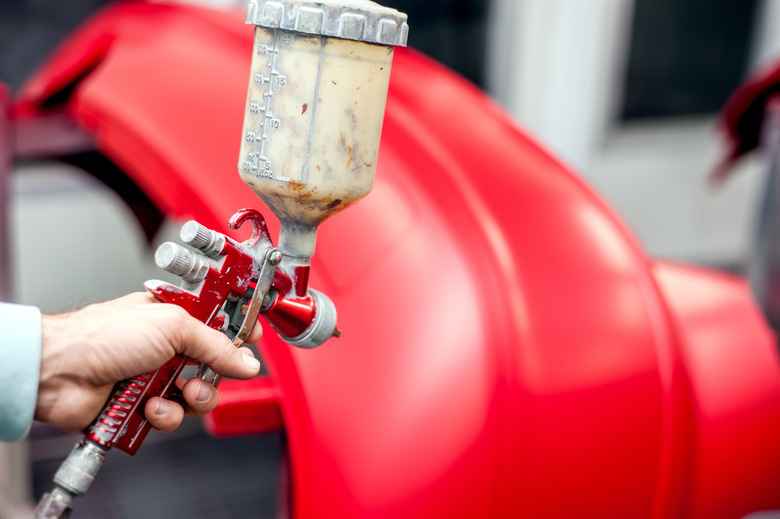 Close-up of spray gun with red paint painting a car