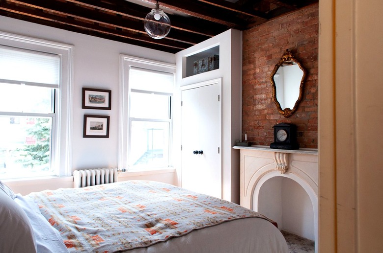 a bed with a southwestern patterned in a bedroom with exposed beams, a fireplace and one brick wall