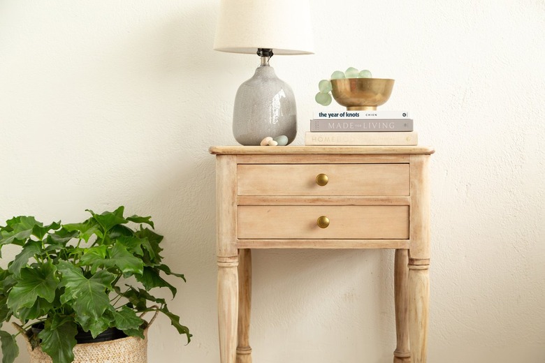 Bleach wood side table next to plant, with a lamp and books